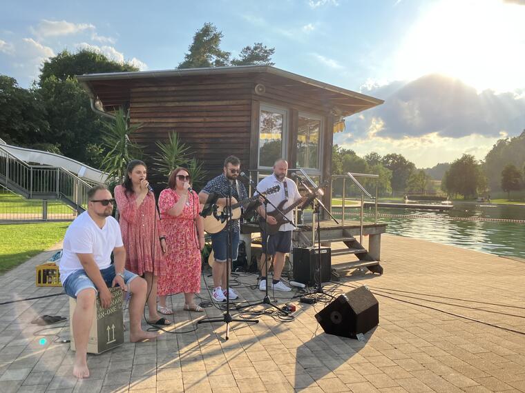 Man sieht die Band, 5 Personen, mit Sonnenschein im Hintergrund